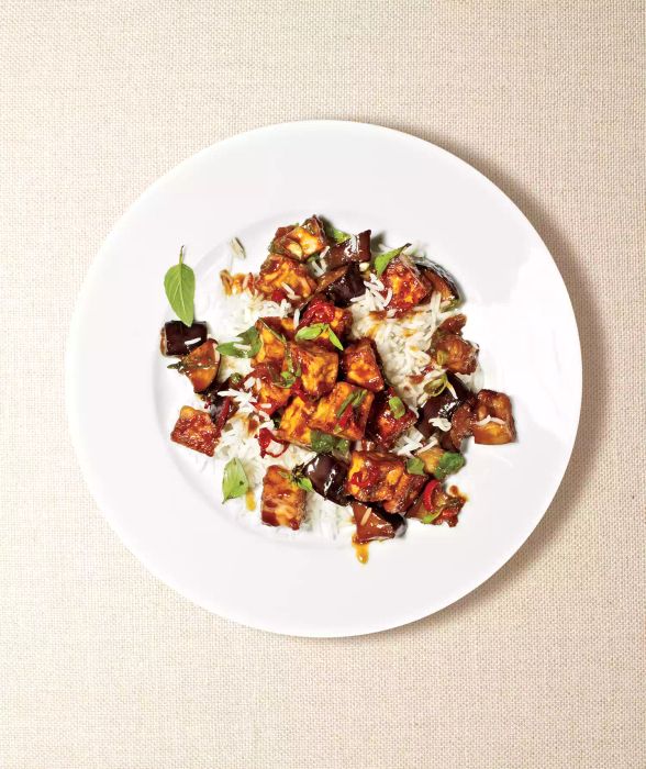 Eggplant and tofu stir-fry served on a white plate, topped with torn basil leaves.