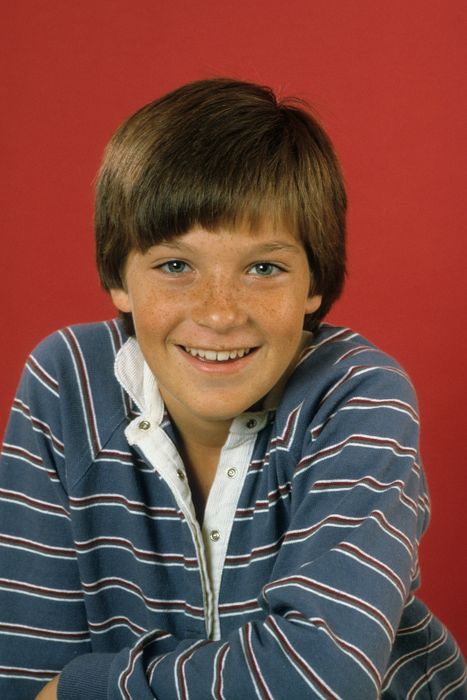A teenager in a striped shirt beams in front of a simple background