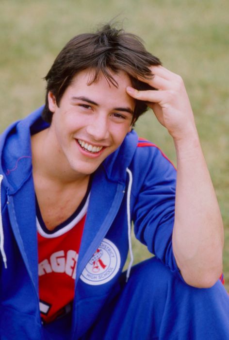 A person beaming outdoors, dressed in an athletic tracksuit and a sports jersey