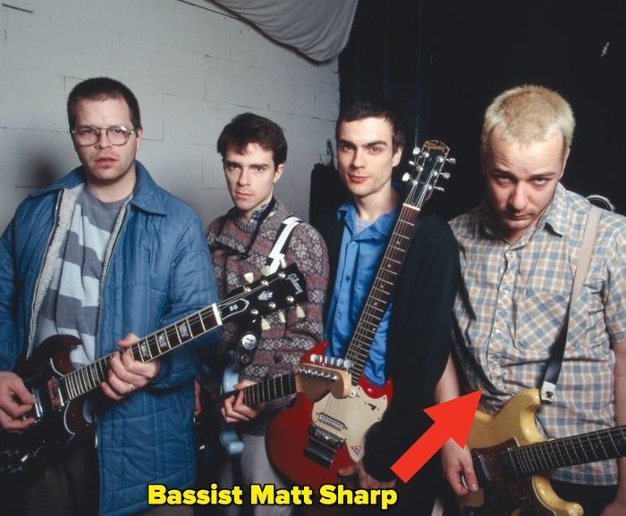 A group of four people with guitars casually pose in a studio, dressed in relaxed and patterned outfits