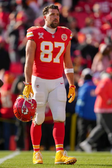 In full football gear, Travis holds his helmet while standing on the field, ready for action.