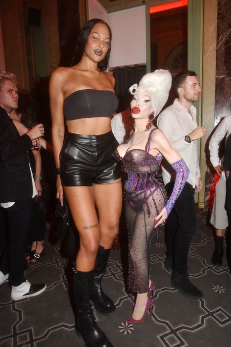At a star-studded event, Liz is seen in a strapless top paired with leather shorts, while Amanda stuns in a rhinestone bodysuit and bold hairstyle. In heels, Amanda’s height reaches just up to Liz's chest.