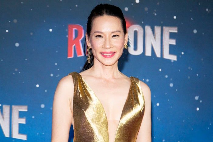 Lucy Liu shining on the red carpet in a stunning gold gown, smiling with confidence.