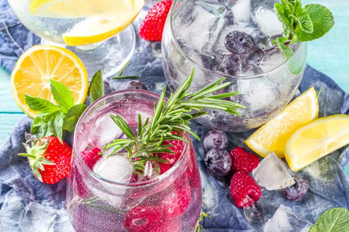 Summer beverage idea. Fruit-infused gin and tonic or refreshing lemonade mocktails with fresh blueberries, raspberries, lemons, and herbs, set against a weathered blue-green wooden backdrop with ample space for text