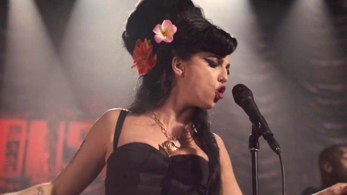A singer performs passionately on stage, wearing a vintage-inspired dress adorned with flowers in her hair, singing fervently into a microphone.