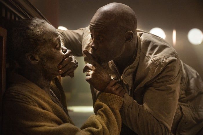 In a tender and serious moment, Djimon Hounsou gently places his hand over Lupita Nyong'o's mouth and signals for quiet with a finger to his lips.