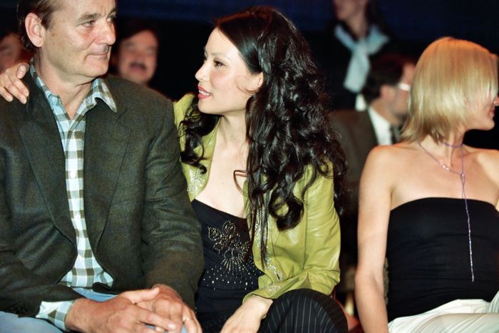 Bill Murray and Lucy Liu sitting together, one in a jacket, the other wearing a patterned top with a jacket, engaged in a conversation at an event.