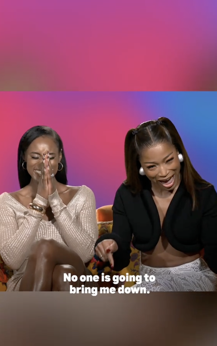 Two women sit together, smiling. One wears a beige sweater dress, while the other sports a black top. The text below reads, "No one is going to bring me down."