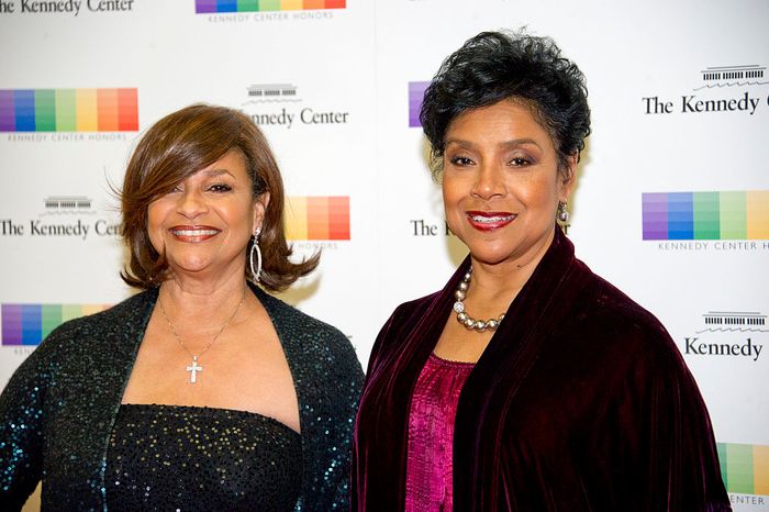 Two women attending the Kennedy Center Honors, both dressed in glamorous evening gowns, smiling at the photographers.