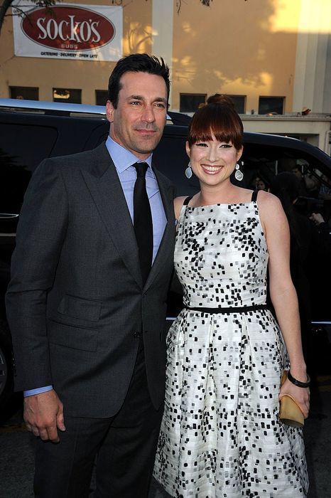 A man in a suit and a woman in a stylish dress, adorned with earrings, posing on a sidewalk