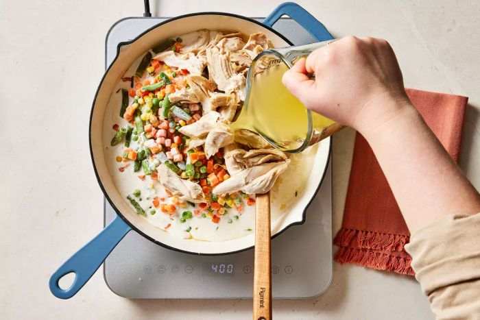 Combining all the filling ingredients for the chicken pot pie in a pot with broth