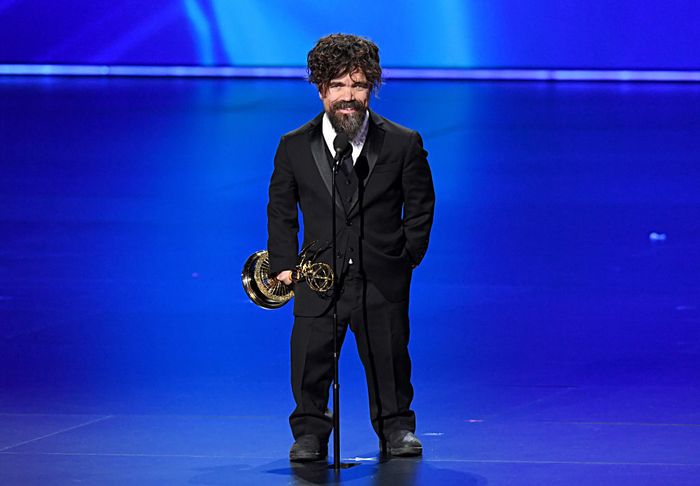 A person dressed in a suit, holding an award, standing on stage and delivering a speech.
