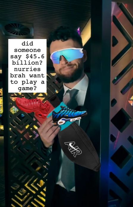 A person in a suit, wearing reflective sunglasses, holds two sneakers and an 'AIR' branded bag while standing in front of a modern, patterned backdrop.