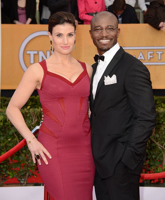 Taye in a tuxedo and Idina in a sleek gown strike a pose on the red carpet at a celebrity event.