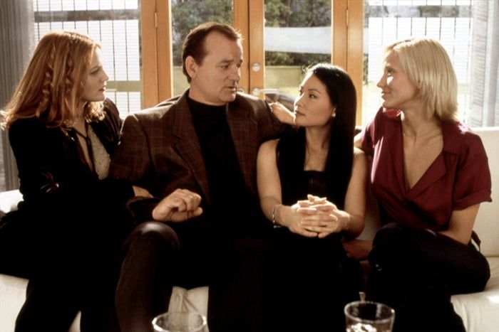 Drew Barrymore, Bill Murray, Lucy Liu, and Cameron Diaz casually chatting on a couch, dressed in fashionable, relaxed outfits in a cozy living room space