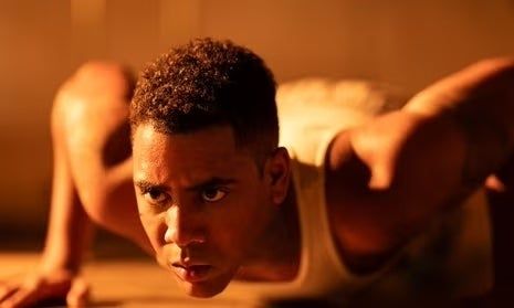 A person, deeply focused and wearing a sleeveless shirt, appears primed for action in an emotionally charged scene.