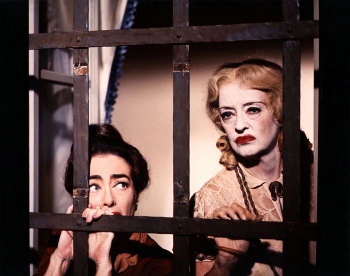 Joan and Bette look anxiously through barred windows, their expressions filled with concern.