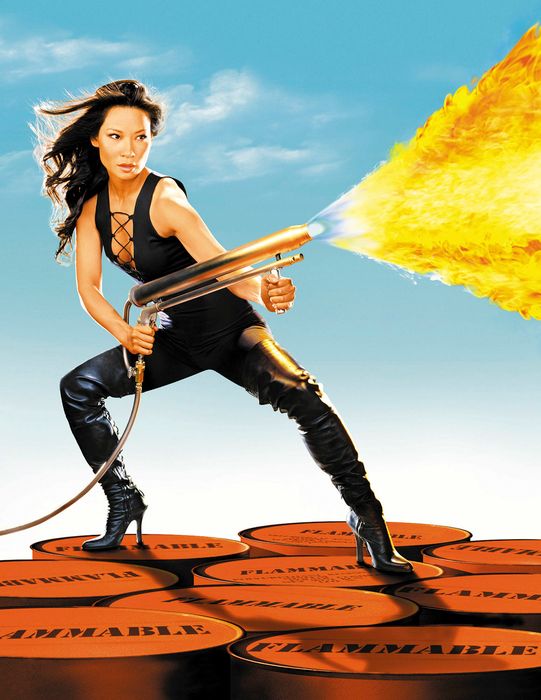 Lucy Liu posing with a flamethrower on top of stacked barrels marked 