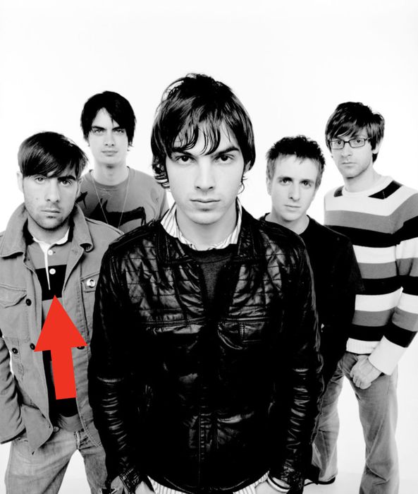 Five men stand together, one in a leather jacket positioned at the front. The photo has a casual, black-and-white vibe.