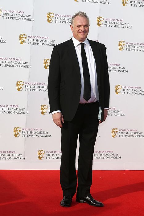 Greg, dressed in a sharp suit, smiles as he poses on the red carpet at an awards ceremony, with the event's branding in the background.