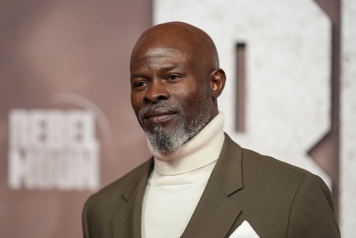 Djimon Hounsou sporting a tan suit and a white turtleneck at a high-profile celebrity event.