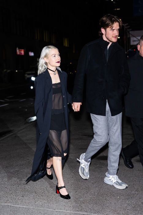Phoebe and Bo stroll together, with Phoebe wearing a sheer dress, a long coat, and heels, while Bo sports a dark jacket and light pants. Even in heels, she doesn't quite reach his shoulder.