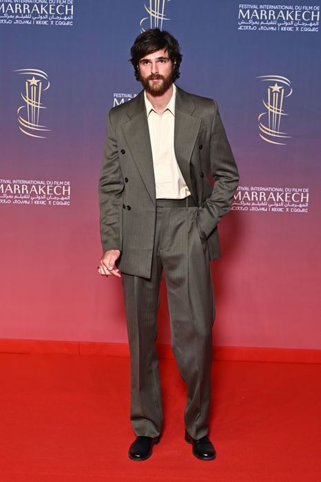 Jacob, dressed in a tailored suit, strikes a pose on the red carpet at a film festival event.