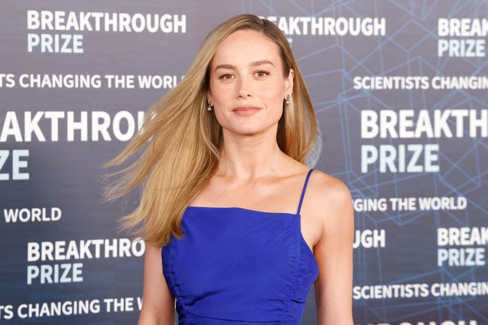 A person in an elegant blue gown poses on the red carpet at the Breakthrough Prize event, with event branding in the background.