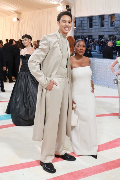 Brittney and Cherelle pose on the red carpet. Brittney is dressed in a long coat and suit, while Cherelle wears a strapless dress. The elegant event setting serves as a backdrop, with Cherelle reaching just up to Brittney's chest.