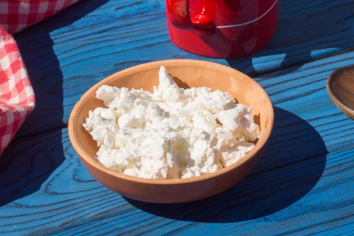 A basket with a cup of milk and a portion of cottage cheese on a blue wooden table.