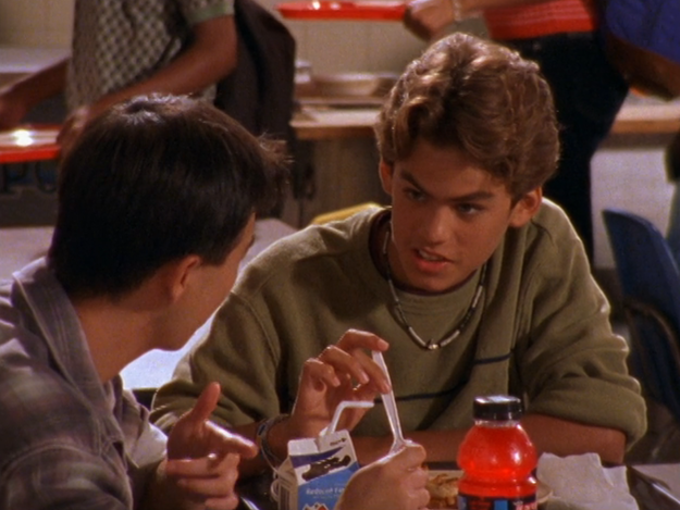 Two people are sitting at a table, chatting. One person holds a straw near a drink. A juice bottle and a milk carton are on the table.