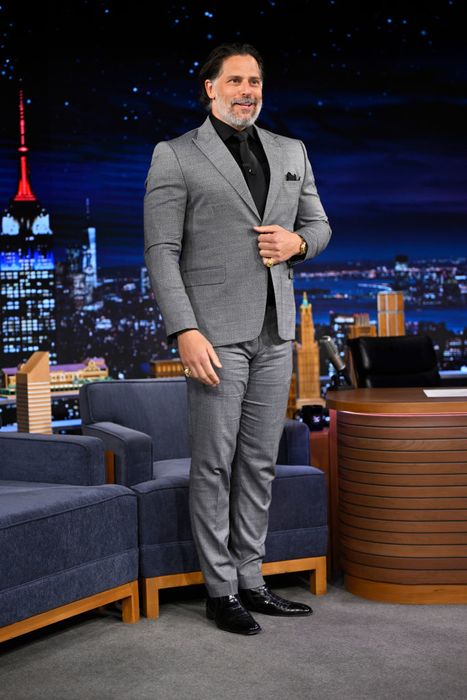Joe, dressed in a sleek suit, stands confidently on a talk show set with a glowing cityscape backdrop behind him.