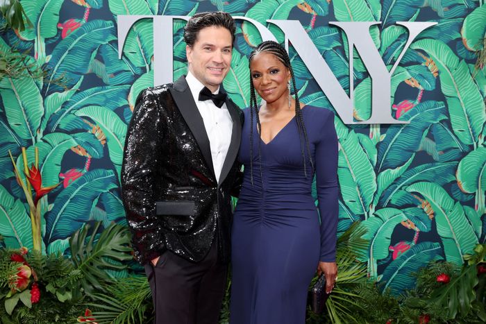 Will, dressed in a sequined tuxedo, and Audra, in a graceful ruched dress, pose together at a formal event with a tropical-themed backdrop.