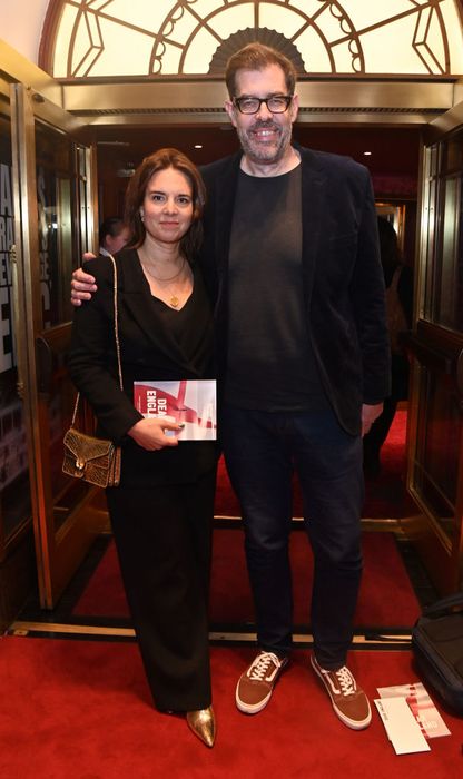 Ingrid and Richard pose together at the event: she wears a flowing dress and holds a booklet, while he sports a casual look with glasses and sneakers. Ingrid’s height reaches just above Richard's chin.