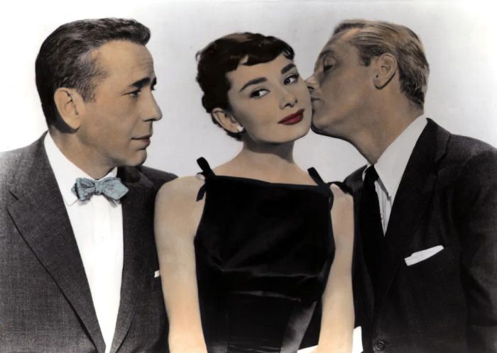 Humphrey watches as William kisses Audrey's cheek, all three dressed in formal attire.