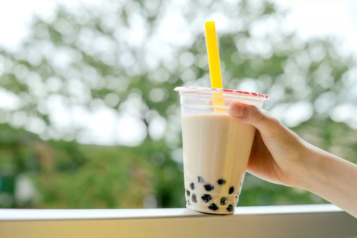 A human hand holding a cup of iced bubble tea with milk and tapioca pearls