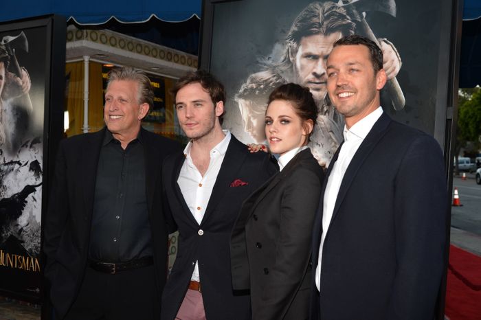Four individuals in formal attire pose at a movie premiere in front of a film poster.