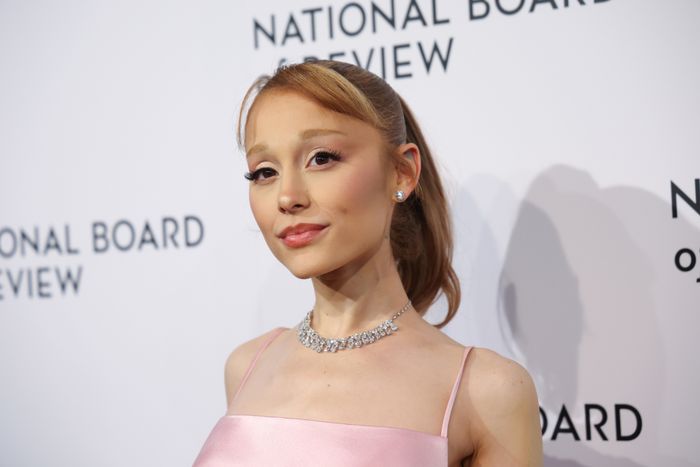 Ariana Grande, wearing a satin gown and diamond necklace, poses confidently at the National Board of Review event.