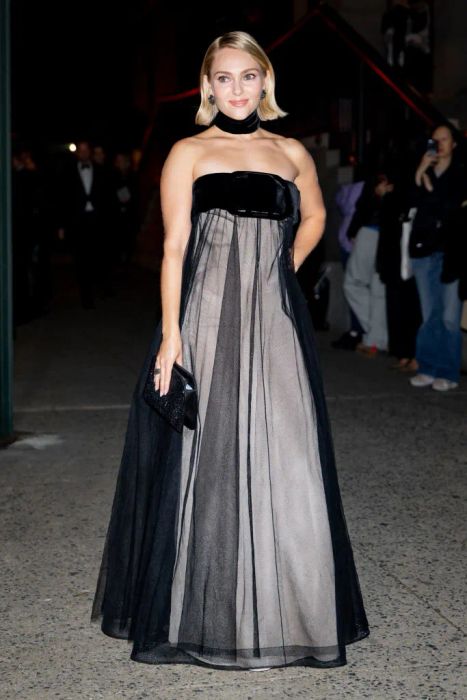 AnnaSophia is seen on the red carpet, wearing a sheer gown with a strapless velvet bodice and a choker, holding a clutch, while people are visible in the background.