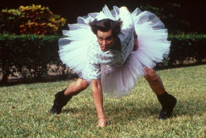 A person crouches on the grass, wearing a tutu and a patterned shirt, their expression showing intense focus as they prepare for something important.