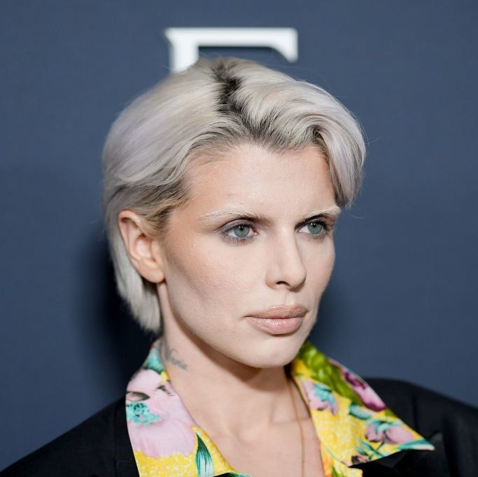 A person with short hair wears a colorful floral shirt beneath a dark blazer at a celebrity event.