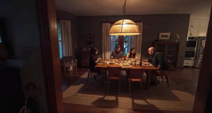 A cozy and intimate atmosphere unfolds as people gather around a table beneath a large, glowing hanging lamp, enjoying the warmth of the room.