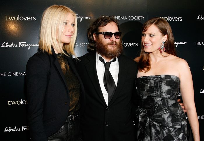 Three individuals strike a pose at a 'Two Lovers' event. The person on the left wears a blazer, the one in the middle sports a suit and sunglasses, and the person on the right is in a strapless dress.