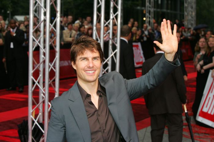A person in a suit waves on the red carpet, surrounded by a crowd and event staff.