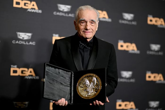 A person in a black suit is holding a large award plaque at the DGA Awards.