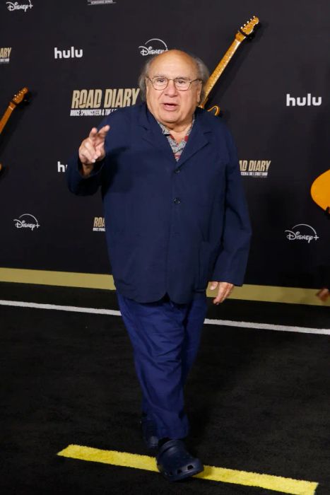 Danny, dressed in a casual suit and Crocs, strikes a pose on the red carpet at a