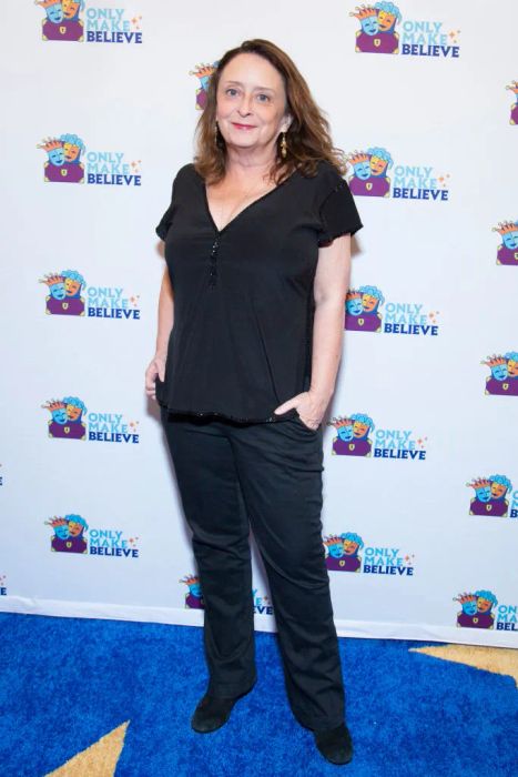 Rachel poses in a casual outfit in front of a backdrop for the