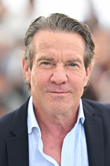 Dennis Quaid, dressed in a suit jacket and striped shirt, gazes at the camera with a calm expression.