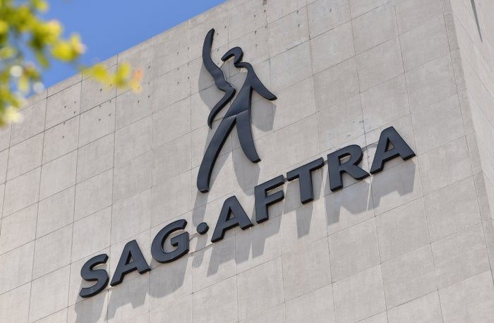 The SAG-AFTRA logo, featuring a stylized human figure along with the organization's name, is displayed on a concrete building wall.