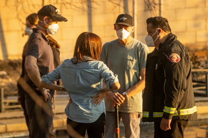 A group of individuals, including a firefighter and others wearing masks, engaging in conversation outdoors in a casual setting